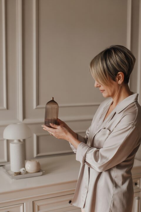 40+ woman with pixie highlighted hair thoughtfully holding a decorative item in a calm, minimalist living space.